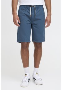 Pantalones cortos casuales azules hechos de tejido ligero. Cuentan con una cintura de cordón con detalles de cuero. A la altura de la rodilla y con una textura suave.