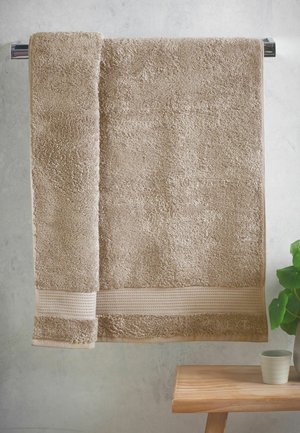 Serviette beige pliée suspendue à une barre argentée au-dessus d'un banc en bois avec une petite tasse blanche et une plante verte à proximité.