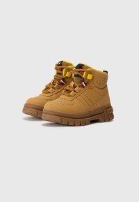 Bottes montantes beiges avec tige en textile et synthétique, col rembourré, lacets jaunes contrastants et semelle en caoutchouc nervurée. Présente des accents de logo.