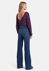 Maglione viola a lavorazione ondulata con scollatura a V profonda, abbinato a jeans blu a gamba larga a vita alta con orlo arrotolato e tasche posteriori.