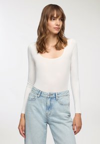 Body in bianco a maniche lunghe con scollo quadrato abbinato a jeans in denim azzurri a vita alta. Tessuto morbido e liscio.