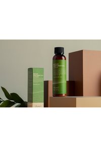 Benton Deep Green Tea Lotion i en mörk flaska med en grön etikett, visad bredvid en matchande låda, på varierande bruna geometriska ytor.