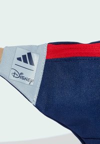 Námořnický batoh s červenými a šedými akcenty, vyrobený z texturované látky, skládající se z vrstvených materiálů, s logy Adidas a Disney na nášivce.