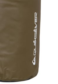 Bolsa marrón resistente al agua con una textura suave y una base negra, que presenta un logo blanco en el lateral. Forma cilíndrica con diseño sellado.