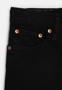 Jeans in denim nero con rivetti color rame, una tasca frontale e una superficie in tessuto testurizzato, evidenziando durevolezza e stile.