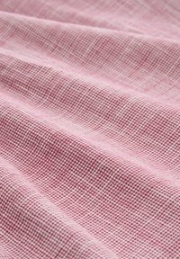 Tissu texturé de couleur rose clair avec un motif à carreaux, présentant de douces plis et vagues, mettant en avant son tissage et sa douceur.