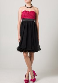 Särlös klänning med rosa blommig brodyr på bodyn, svart flödande kjol med volangkant, tillsammans med klarröda högklackade skor.