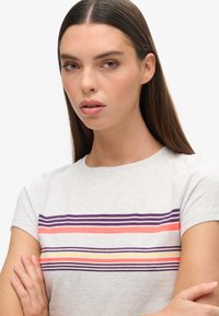 Camiseta de manga corta gris claro con rayas horizontales en púrpura, naranja y amarillo. Tejido suave con escote redondo y corte relajado.