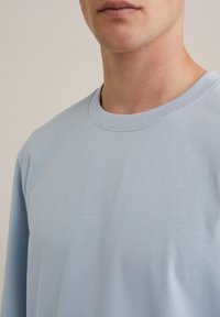 Helles blaues T-Shirt mit kurzen Ärmeln, Rundhalsausschnitt, aus glattem Baumwollstoff, mit minimalen Nähten und entspanntem Schnitt.
