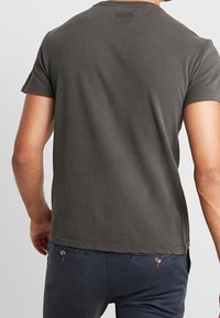 Šedé bavlněné tričko s krátkými rukávy, kulatým výstřihem a volným střihem. Výrazné prošití a bezešvý lem na rukávech a spodním okraji.