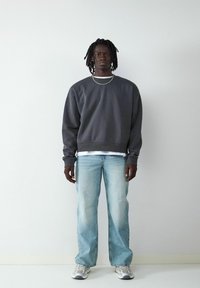 Ciemnoszara bluza o luźnym kroju, warstwowo noszona na białej koszuli, zestawiona z jasnoniebieskimi spodniami w stylu wide-leg i szarymi trampkami.