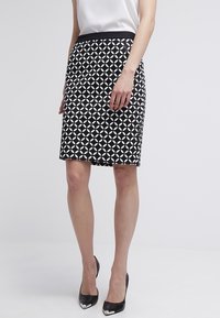 Black and white patterned pencil skirt with geometric design; fitted shape, smooth fabric, and a solid black waistband. Paired with high heels.