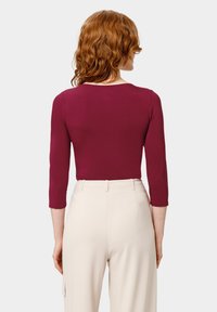 Haut bordeaux à manches longues avec un col rond, associé à un pantalon beige clair ajusté avec des poches latérales et une coupe droite.