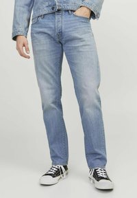 Vaaleansiniset slim fit -farkut, joissa on klassinen viisi taskua -design ja kulunut pinta, yhdistettynä musta-valkoisiin tennareihin.