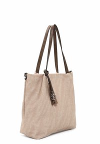Beige fabric tote bag with two brown leather straps, featuring a tassel accent and a silver hardware logo detail. Smooth texture overall.
