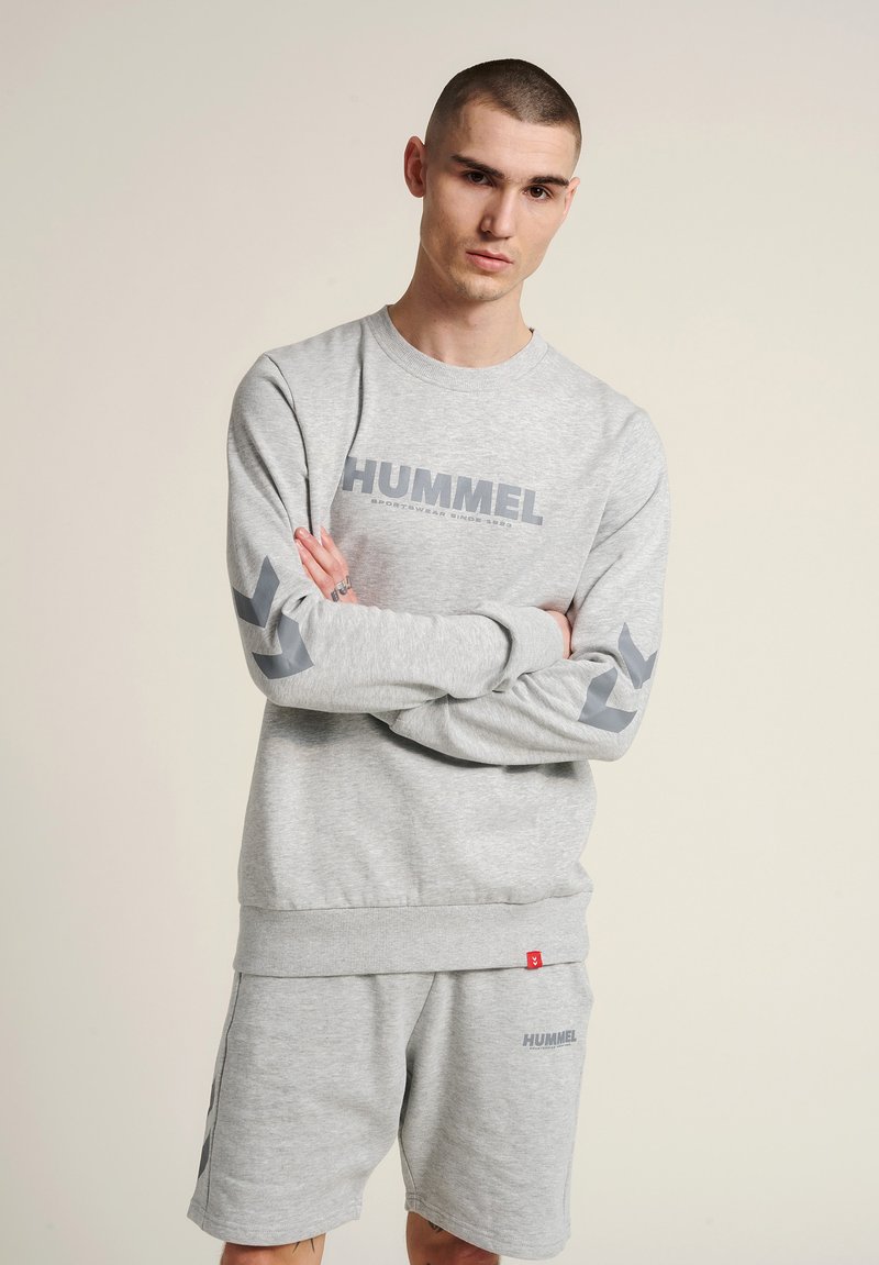Szary sweatshirt z logo "HUMMEL", prążkowany dekolt i szare akcenty w kształcie chevron na rękawach, w zestawie z dopasowanymi szarymi szortami.