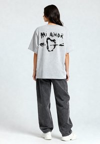 T-shirt gris surdimensionné avec un texte et un design graphique noir au dos, associé à un pantalon gris foncé et des baskets blanches.