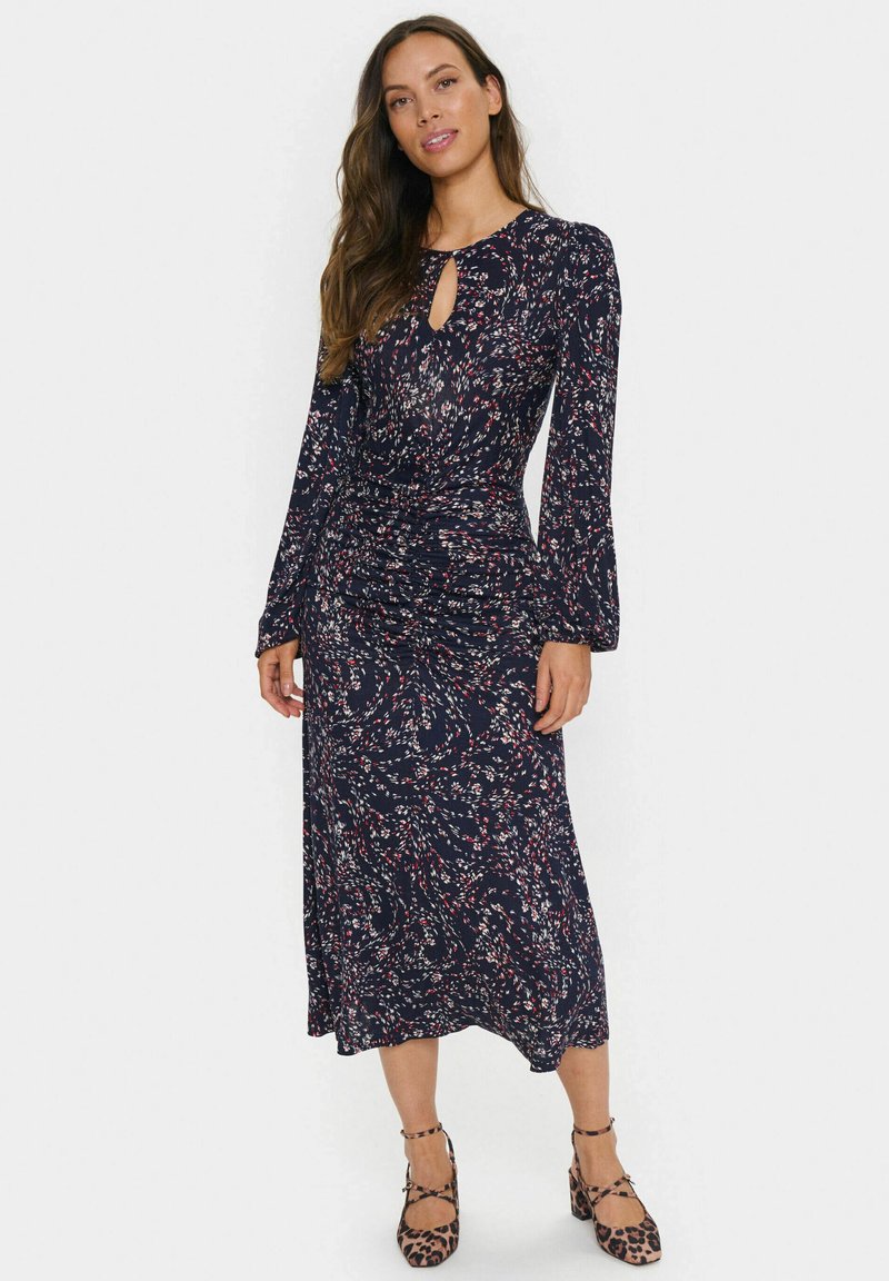 Langärmliges, dunkelblaues Kleid mit floralem Muster in Rot und Weiß. Verfügt über einen Schlüssel-Ausschnitt und geraffte Details an der Taille.