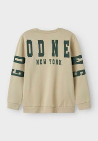 Beiger Pullover mit grünen Blockbuchstaben "GOD NEW YORK" auf dem Rücken und den Ärmeln. Gerippte Bündchen und Saum, weiche Textur.