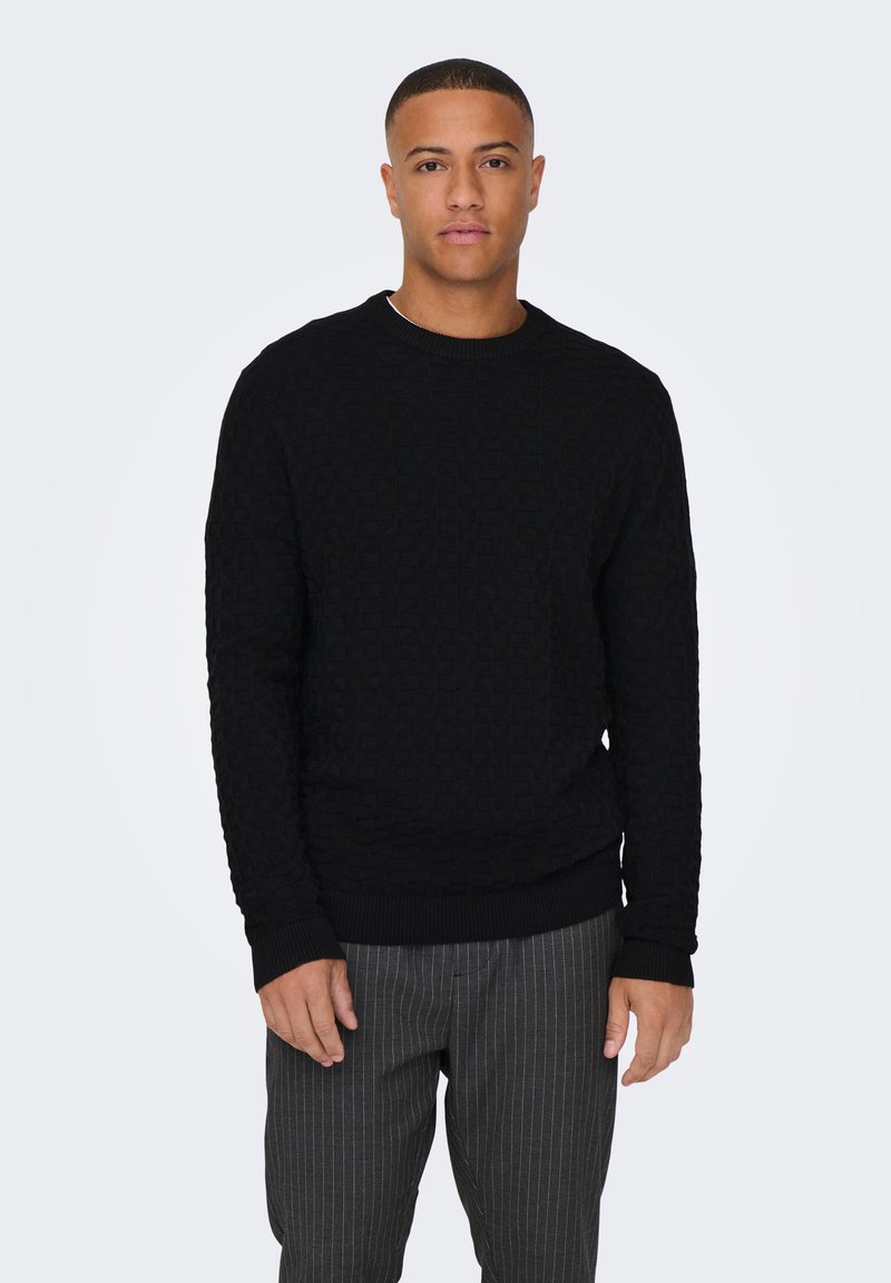Schwarzer strukturierter Pullover mit Rundhalsausschnitt, gerippten Bündchen und Saum. Kombiniert mit grauen Nadelstreifenhosen. Einfaches, lässiges Design.