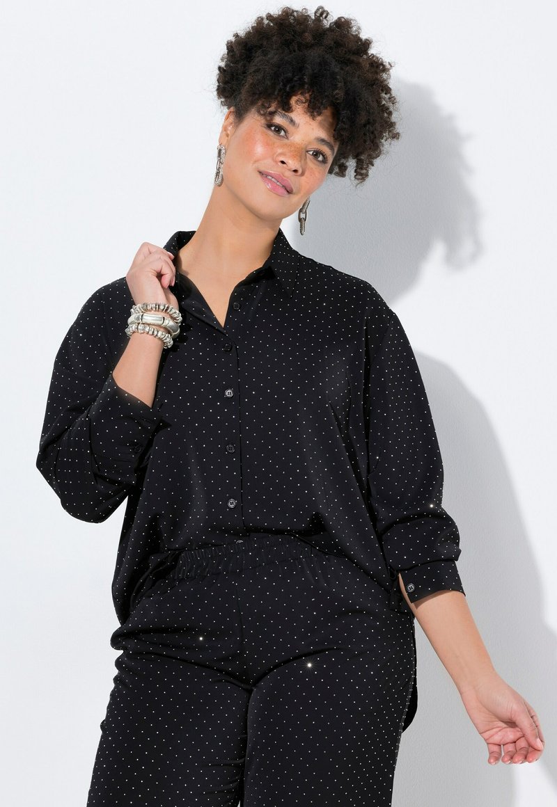 Blusa nera con pois bianchi, dotata di una patta con bottoni, maniche lunghe e vestibilità relaxed. Tessuto morbido con un leggero lucido e pantaloni con vita elastica.