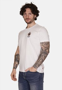 T-shirt in cotone bianco con stampa del logo sul davanti, scollo rotondo e maniche corte. Indossato con jeans denim blu.