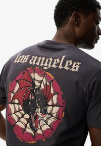 Sort kortærmet t-shirt med et farverigt grafisk design af en panter med edderkoppedesign og "Los Angeles" tekst på ryggen.