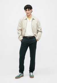 Šviesiai smėlinis bomber tipo švarkas, baltas megztinis, geltonas apykaklė, tamsūs džinsai, žaliai balti sportbačiai su rudais padais. Kasdienis drabužių derinys.