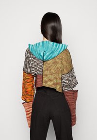 Krótkie, wielokolorowe hoodie z teksturowanym wzorem. Posiada niebieską kapturek w odcieniu aqua oraz różnorodne wzorzyste rękawy w odcieniach brązu, pomarańczy i szarości.