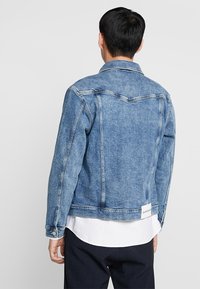 Denimová bunda ve světle modré barvě s mírně opotřebovanou texturou. Obsahuje klasický límec, zapínání na knoflíky na rukávech, zadní yoke a štítek s logem na spodním lemu.