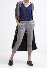 Szary, dziany długi kardigan na granatowej bluzce z dekoltem w serek, szare dopasowane spodnie i czarne buty z detalem klamry.