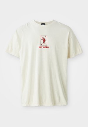 Krémové bavlněné tričko s krátkým rukávem, se středovým červeným grafickým designem postavy a textem "JEN SI DĚLÁM SRANDU!" v červené barvě.