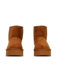 Un paio di stivali corti in suede marrone con suole in gomma spesse, mostrati frontalmente su uno sfondo bianco.