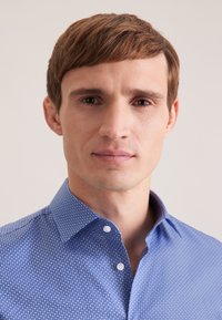 Niebieska koszula w wzory z kołnierzykiem na guziki, ozdobiona małym geometrycznym motywem, gładka w dotyku, wykonana ze średniej grubości materiału.