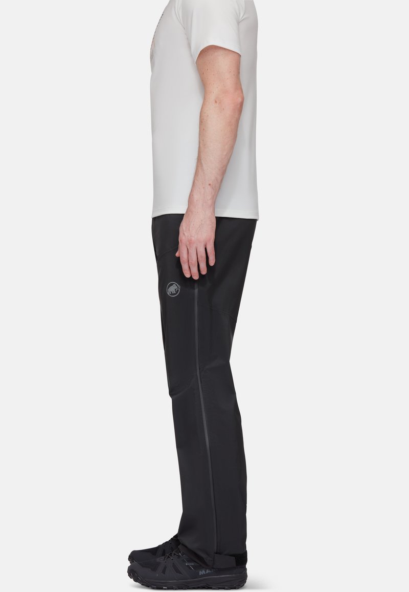 Pantalons noirs d'extérieur à coupe ajustée, fabriqués en matériau synthétique, avec une poche latérale et un détail de logo subtil. Associés à une chemise blanche ajustée.
