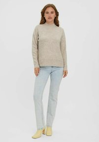 Beige knit sweater with a high neckline, ribbed cuffs, and hem, paired with light blue jeans and yellow block-heeled ankle boots.