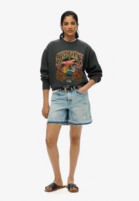 Donkergrijze oversized sweatshirts met grafisch ontwerp; lichtblauwe denim shorts; zwarte sandalen; ontspannen pasvorm, ribbelmanchetten, versleten zoom.