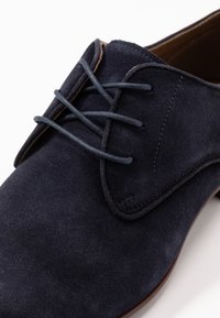 Chaussure en daim navy avec une surface lisse, dotée de lacets étroits et bleu foncé ainsi qu'un bout de chaussure cousu. Design classique avec une forme arrondie.