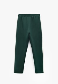 Mørk grønne joggers med en blød tekstur, der har hvide sidelister, en elastisk talje og tapered benåbninger.