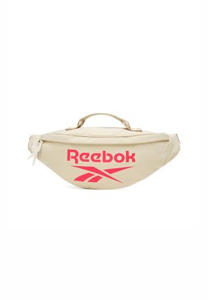 Riñonera beige de Reebok con logo rojo, cierre de cremallera y asa superior, mostrada sobre un fondo blanco.