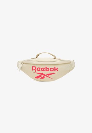 Riñonera beige de Reebok con logo rojo, cierre de cremallera y asa superior, mostrada sobre un fondo blanco.