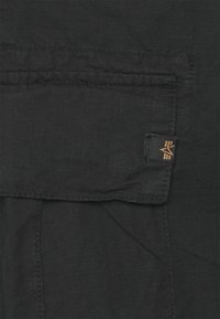 Zwarte stof met een rasterpatroon, met een zak bovenaan en een klein logotagje in koperkleurige stiksel.