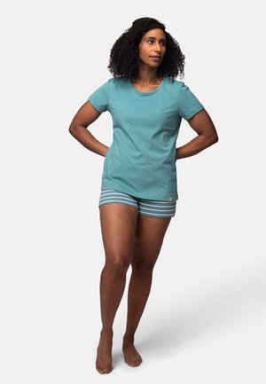 Teal katoenen t-shirt met ronde hals, gecombineerd met gestreepte shorts met blauwe en witte patronen. Model staat blootvoets op een witte achtergrond.