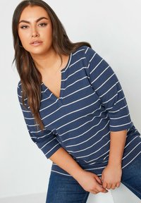 Navy blue, raidallinen pitkähihainen toppi, jossa on V-aukko, valkoiset vaakasuorat raidat ja rento leikkaus. Yhdistetty farkkuhousujen kanssa.