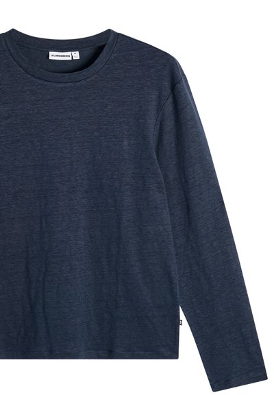 Chemise à manches longues bleu marine avec col rond et étiquette J.LINDEBERG à l'intérieur du col, présentée sur fond blanc.