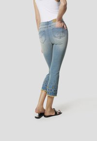 Lichtgewassen denim capri-jeans met bloemrijke borduurwerk aan de zoom, vijf zakken en een rafelige onderkant. Gecombineerd met zwarte slidesandalen.