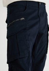 Navy Cargo-Hosen mit mehreren Taschen, einer Reißverschlusstasche an der Seite und einem strapazierfähigen Stoff. Das Design umfasst Nahtdetails und einen geraden Schnitt.