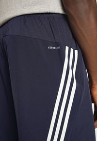 Marina idrottsshorts gjorda av mjukt material, med resårmidja, vita sidostråk och en "AEROREADY"-logotyp på baksidan.