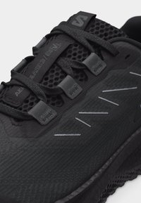 Κοντινή λήψη μαύρου αθλητικού παπουτσιού με πλέγμα στο πάνω μέρος, μαύρα κορδόνια και ασημένια ραφή στο πλάι.