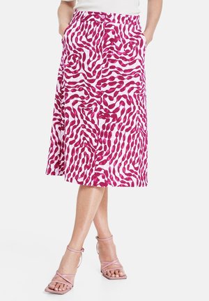 Jupe blanche mi-longue avec un motif abstrait magenta audacieux en spirale, poches avant, fermeture par boutons, portée avec des sandales roses à brides.